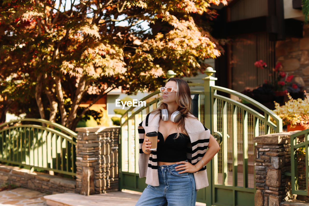 A woman wearing headphones in casual clothes and walks down the street in the countryside in autumn