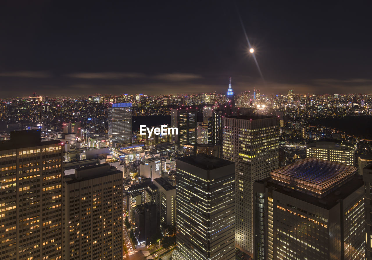Illuminated cityscape of shinjuku  against full moon sky at night