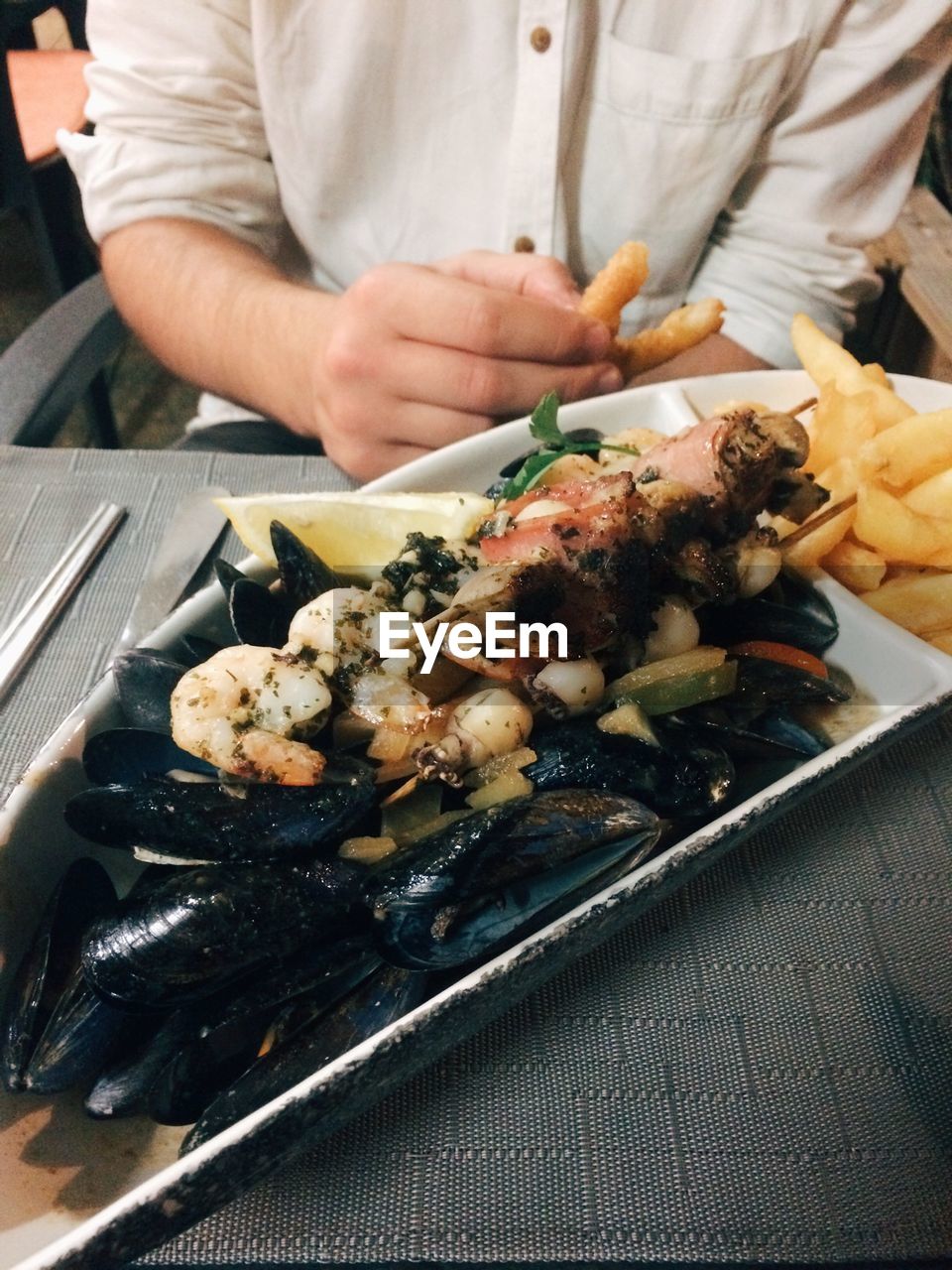 Mussels with prawns and fried fish served in front of man