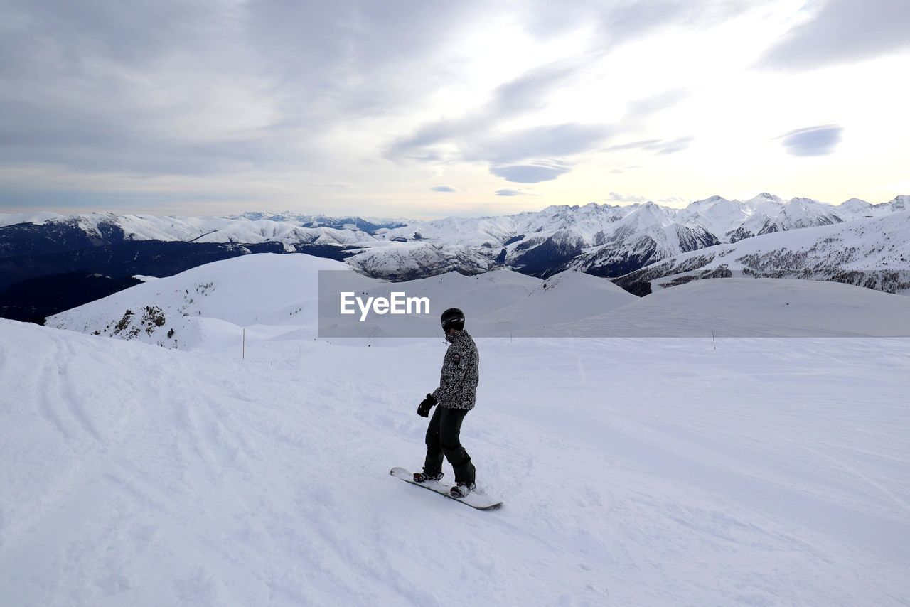 Rear view of snowboarder on snowcapped mountain against sky