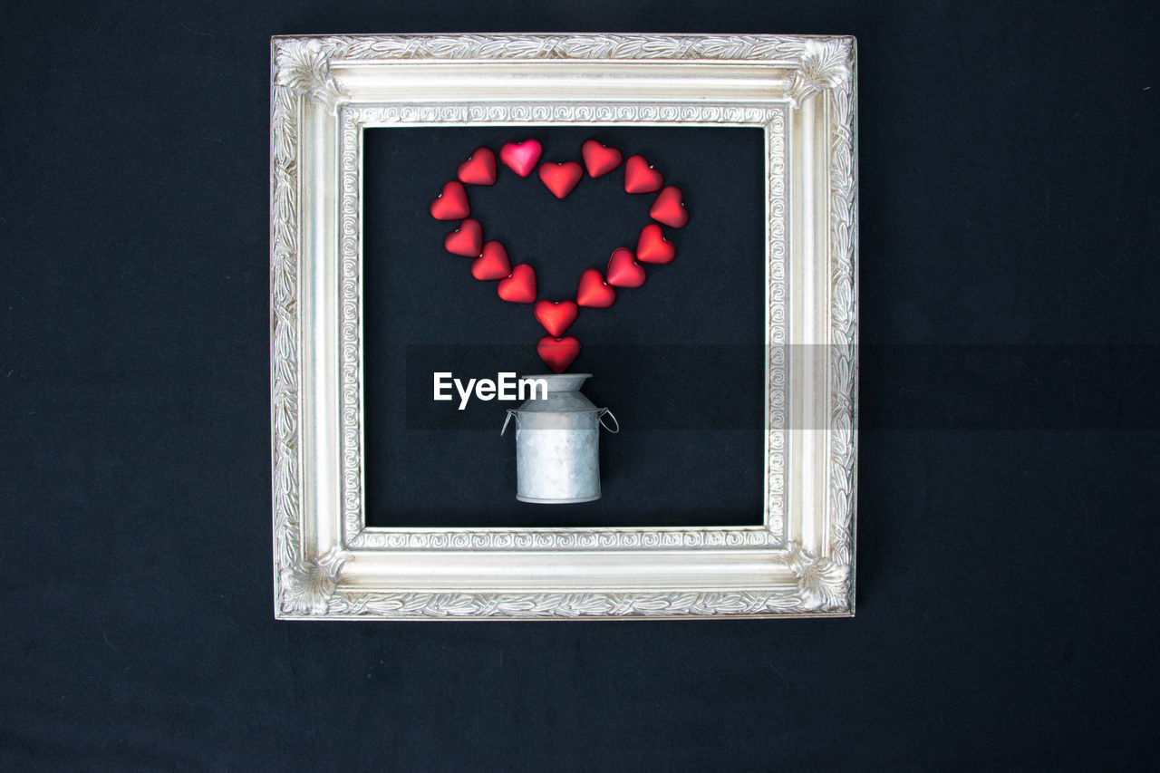Directly above shot of red heart shapes and canister in picture frame on black background