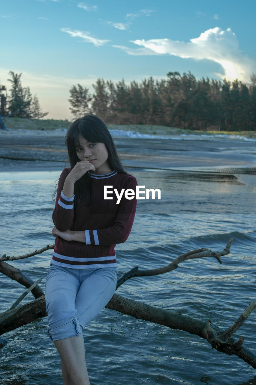 YOUNG WOMAN STANDING ON SHORE AGAINST SKY
