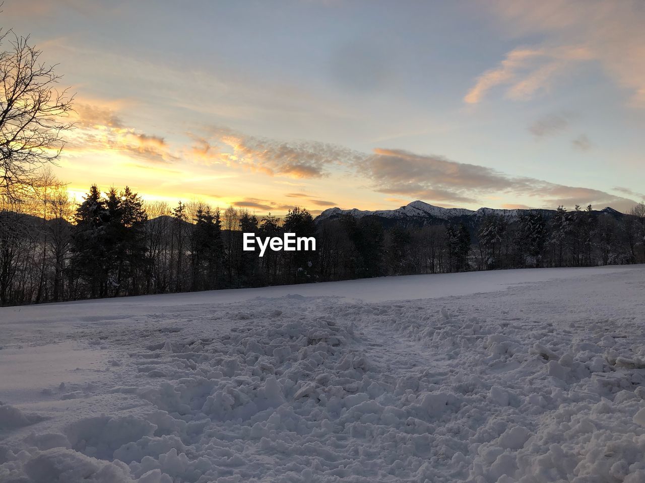 Snow covered field against sky during sunset