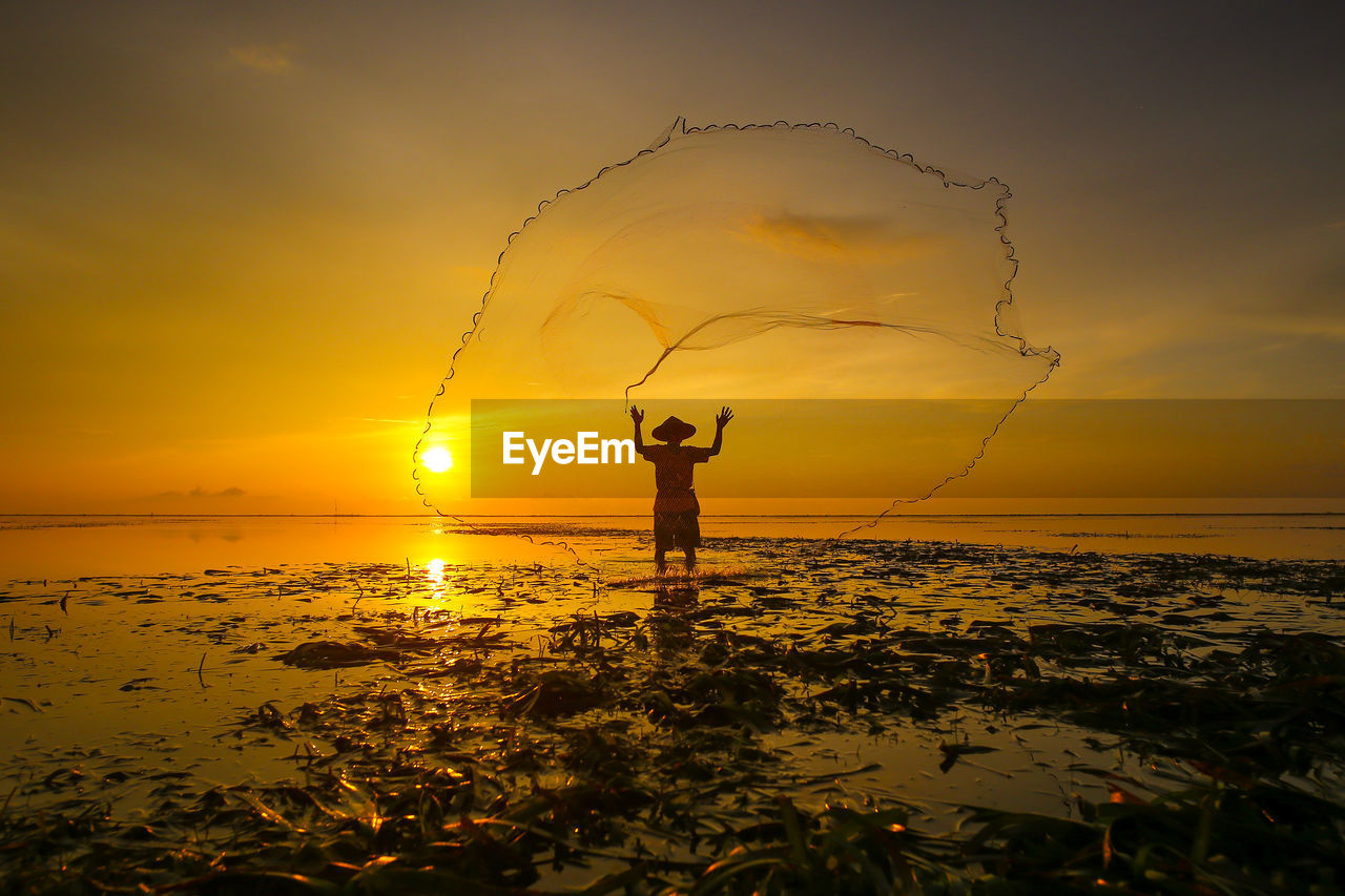 Silhouette man fishing in sea against sky during sunset