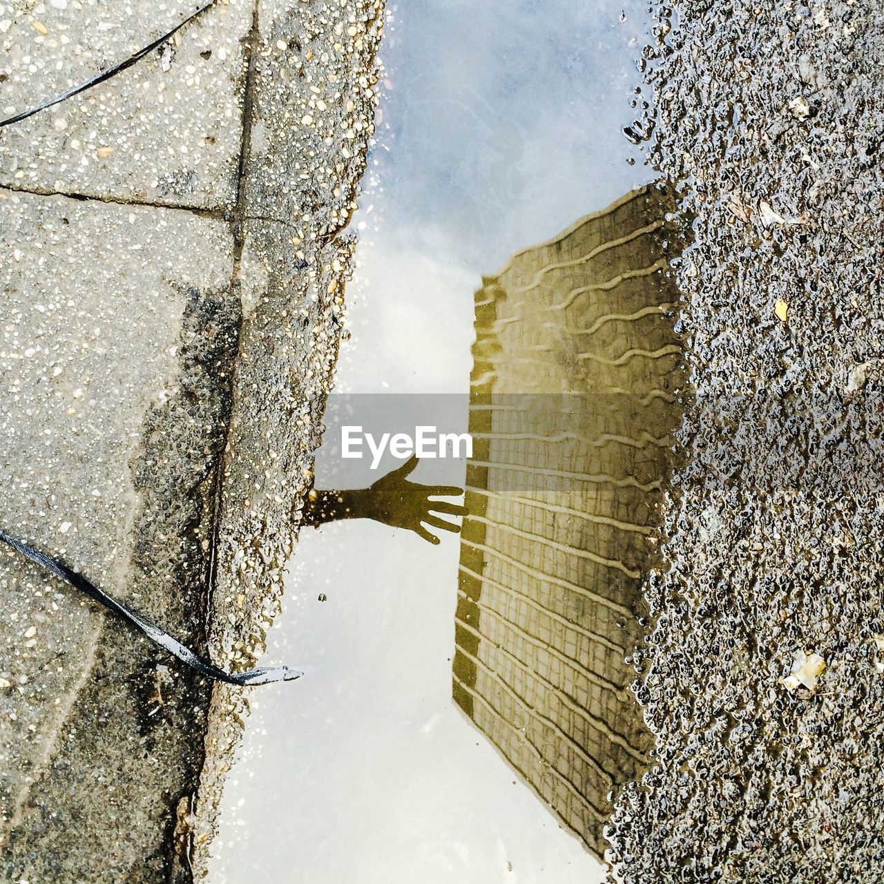 High angle view of silhouette hand and building reflecting on puddle at sidewalk