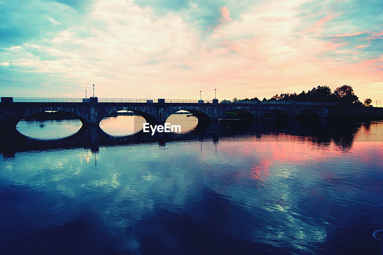 Arch bridge over river against cloudy sky during sunset