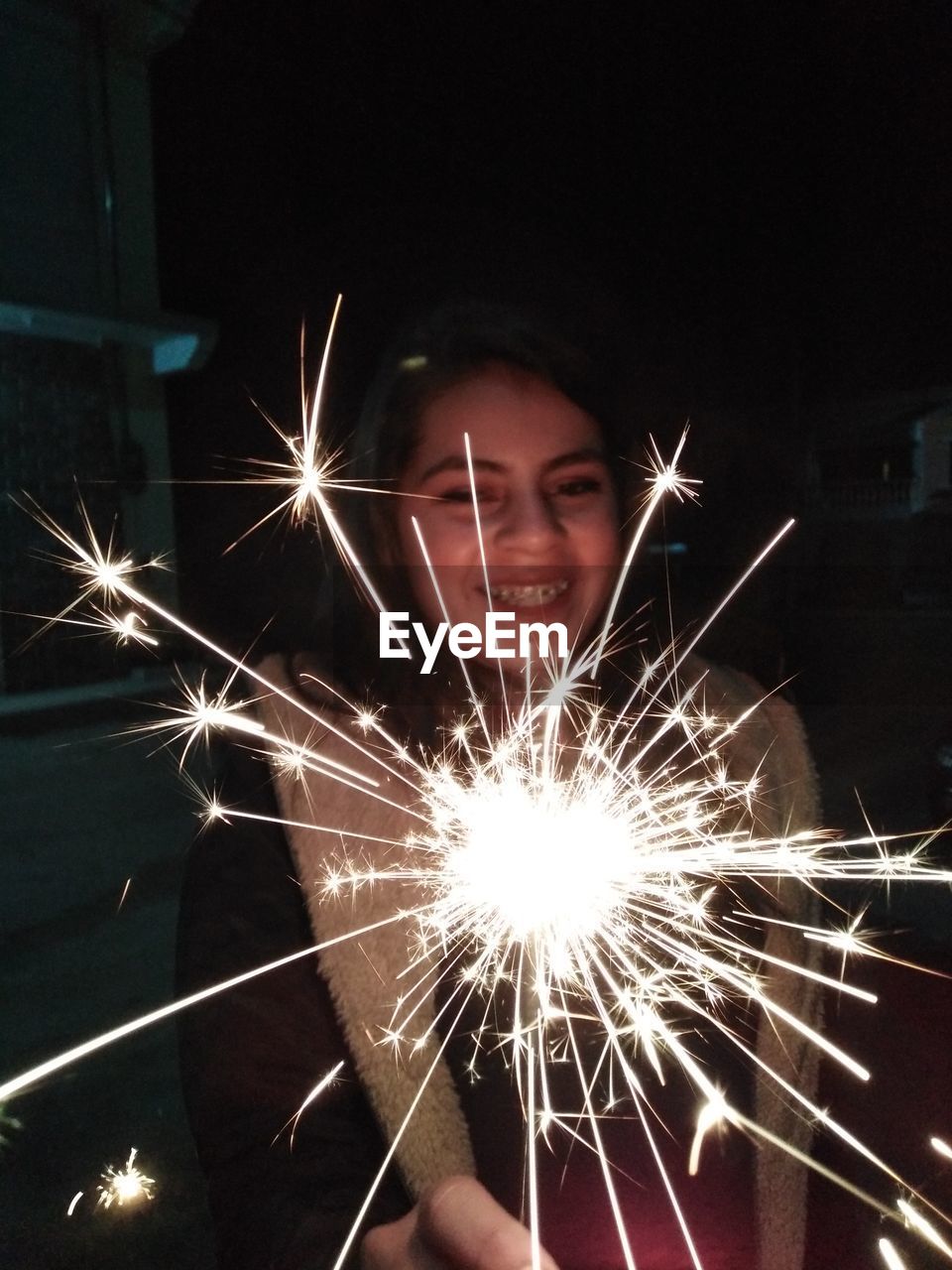 Cheerful teenage girl holding sparkler at night