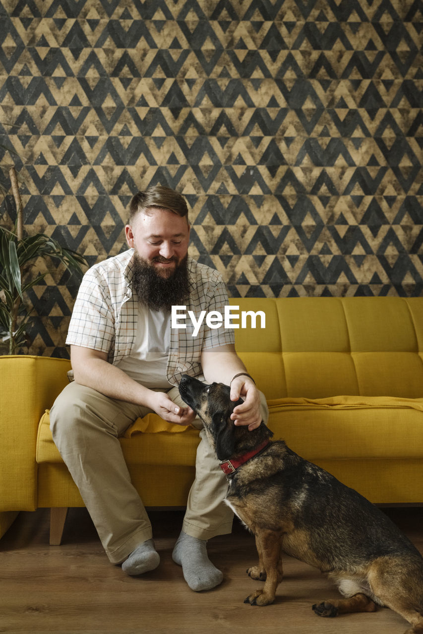 Bearded man stroking dog in living room at home