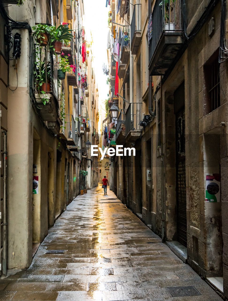 REAR VIEW OF WOMAN WALKING ON COBBLESTONE STREET IN CITY