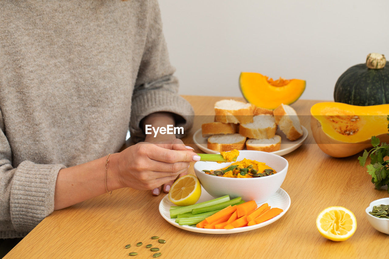 food and drink, food, healthy eating, wellbeing, adult, one person, vegetable, lifestyles, indoors, fruit, women, table, meal, freshness, bowl, orange color, midsection, domestic life, hand, person, men, holding, eating, produce, plate, sitting, casual clothing, salad, home interior, front view, orange, citrus fruit, domestic room, furniture, yellow
