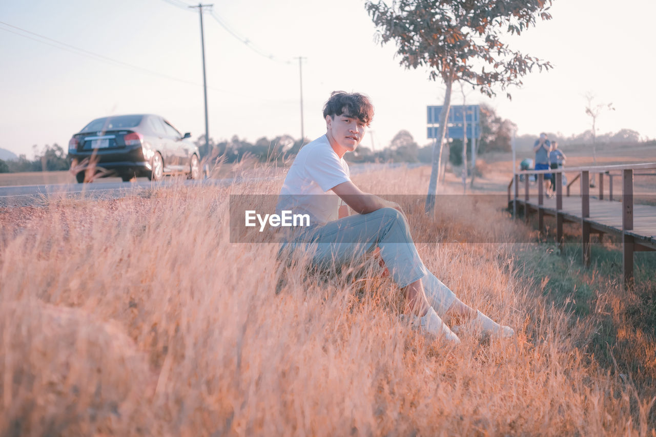 Portrait of man sitting on grassy field by roadside