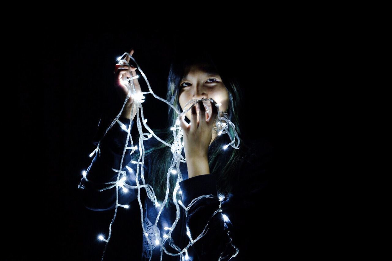 Portrait of woman holding illuminated string lights in darkroom