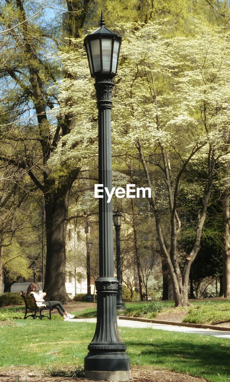 Lamp post by woman sitting on bench at park