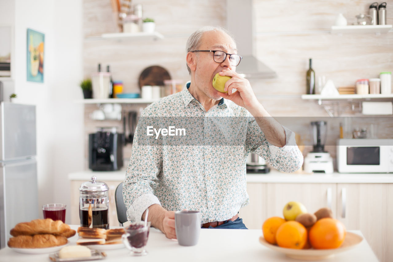 Senior man eating fruits at kitchen