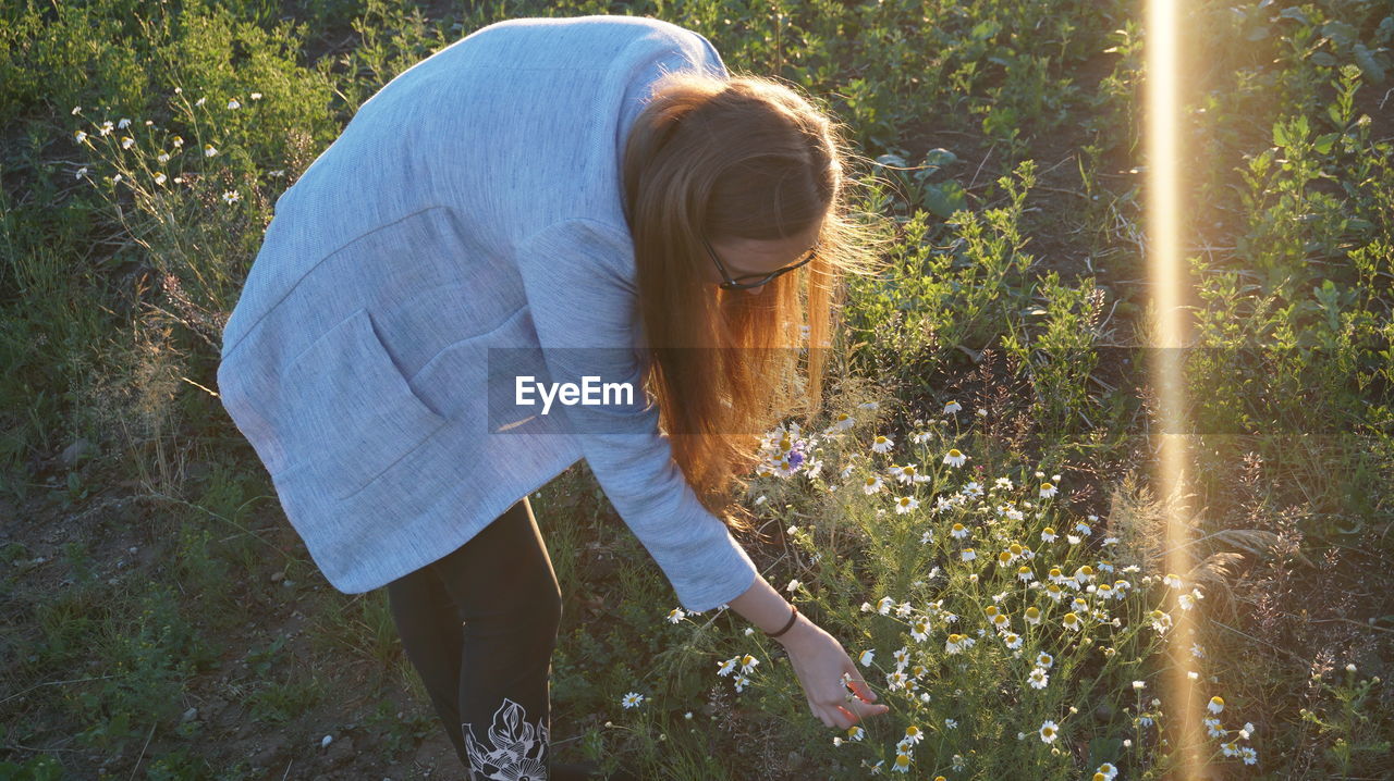 Side view of woman touching while standing by flowering plants
