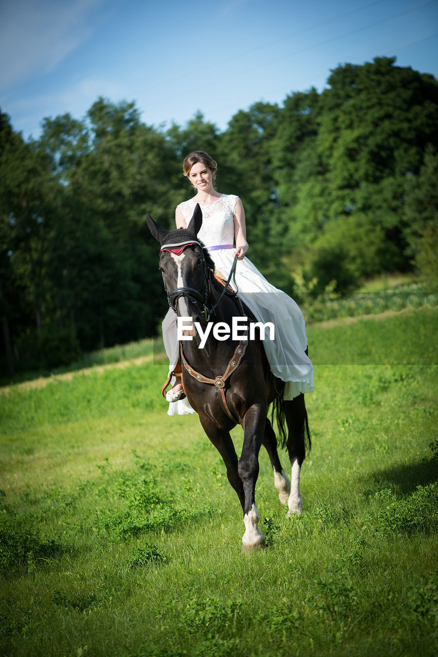 Bride riding horse on grassy field