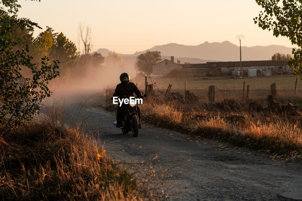 Man in leather jacket and helmet riding bike on asphalt road in sunny autumn day in countryside