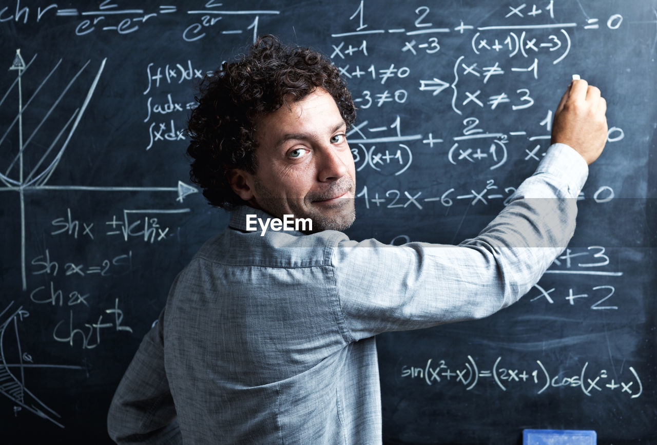 Portrait of teacher writing on blackboard in classroom