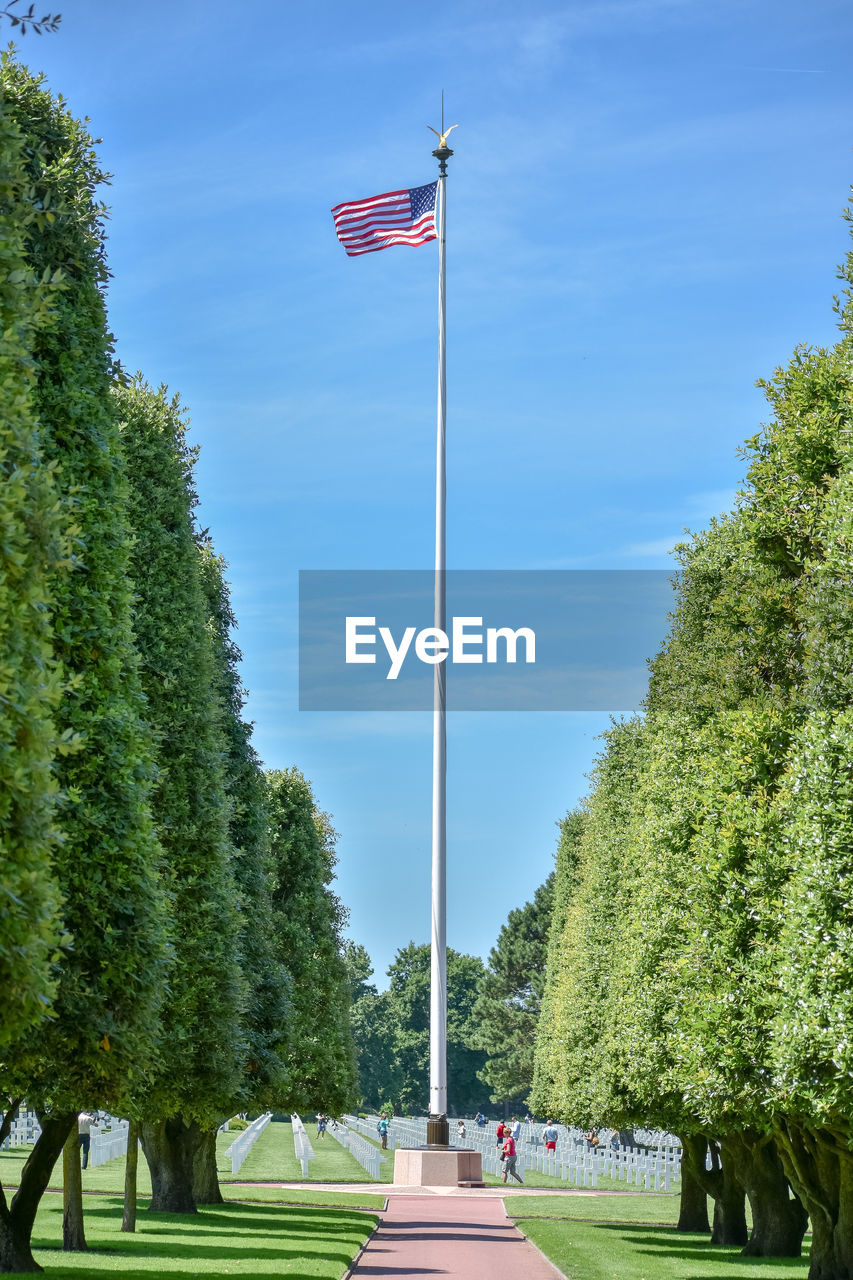 Large united states flag and tourists visiting the garden of the missing at the american cemetery