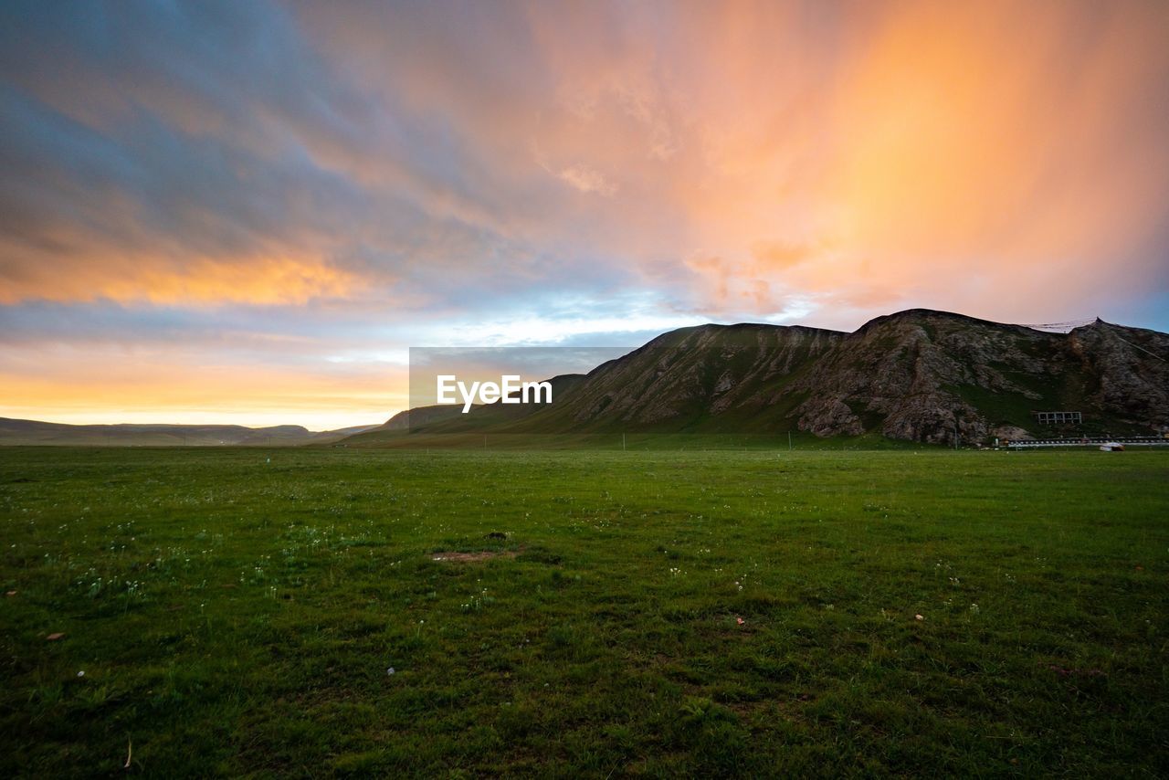 SCENIC VIEW OF FIELD AND MOUNTAINS AGAINST SKY DURING SUNSET