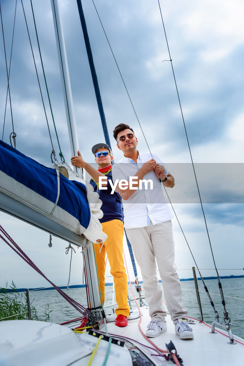 Two young man standing on a sailboat. summer vacations, cruise, recreation