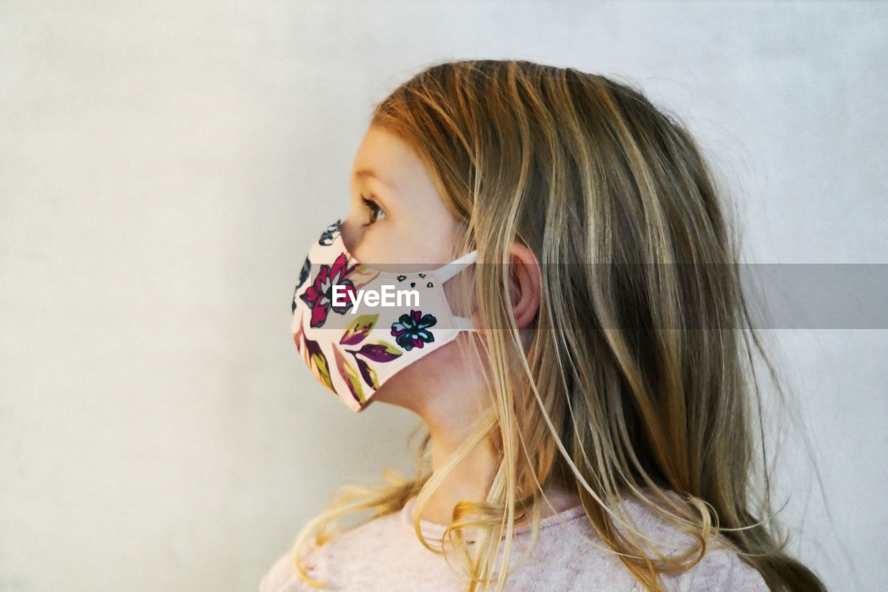 Close-up of cute girl wearing mask standing at home