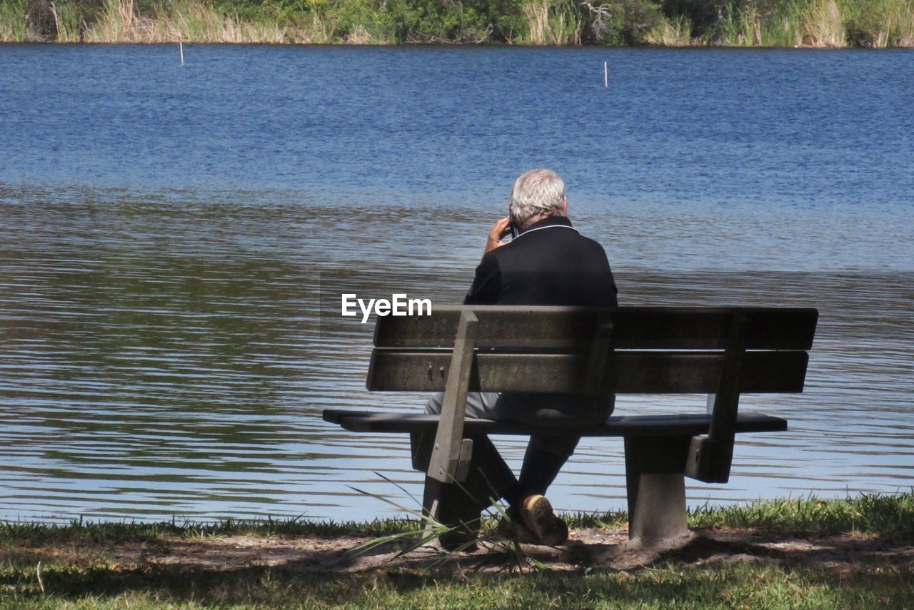 Rear view of senior man sitting on bench by lake