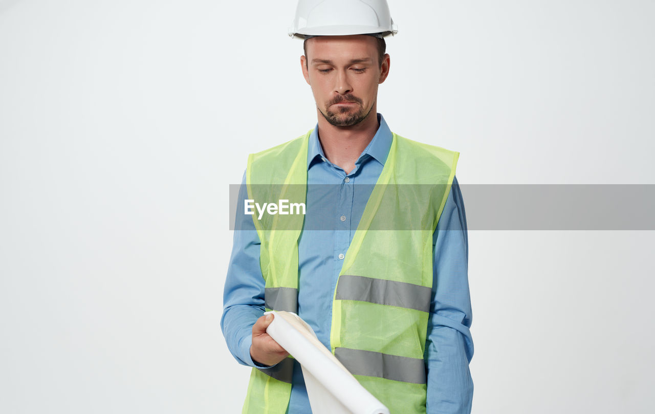 adult, hard hat, occupation, one person, men, reflective clothing, sleeve, construction industry, helmet, headwear, construction worker, working, hat, industry, clothing, construction site, standing, manual worker, protection, studio shot, protective workwear, engineering, business, outerwear, person, indoors, copy space, portrait, front view, dress shirt, white background, building contractor, security, business finance and industry, waist up, looking, looking at camera, serious, professional occupation, beard, expertise, jacket, young adult, businessman, cut out, holding, technology, planning, facial hair, mature adult