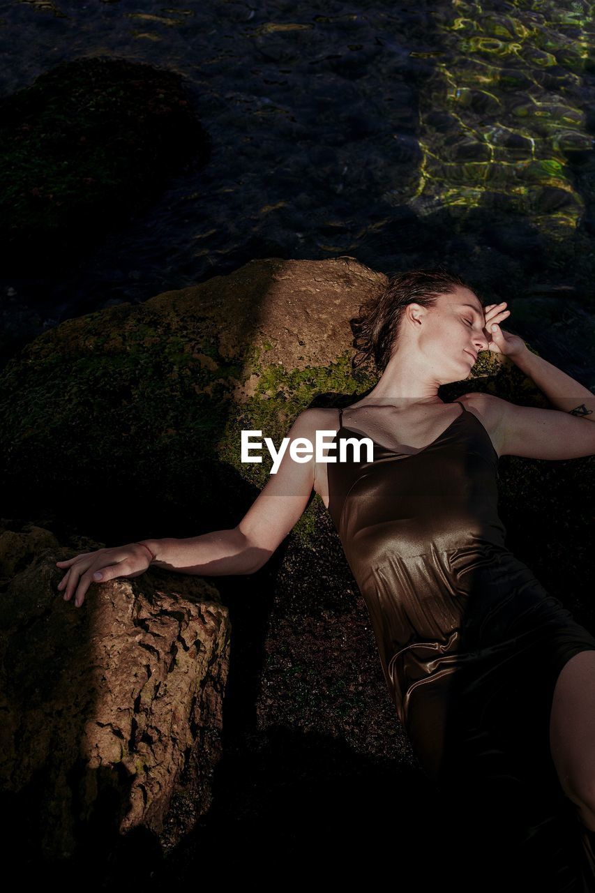 HIGH ANGLE VIEW OF WOMAN SITTING ON ROCK BY LAND