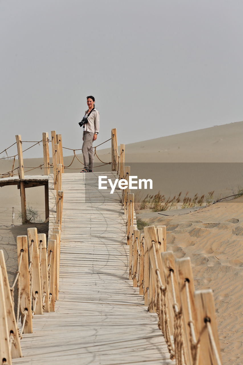 Smiling woman standing on footbridge at desert against clear sky