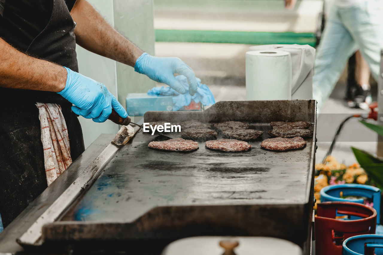 A man fries burger meatballs. man grills some kind of marinated meat on gas grill during summer time