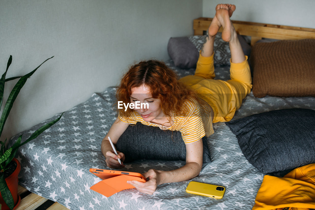 side view of young woman using digital tablet while lying on bed at home
