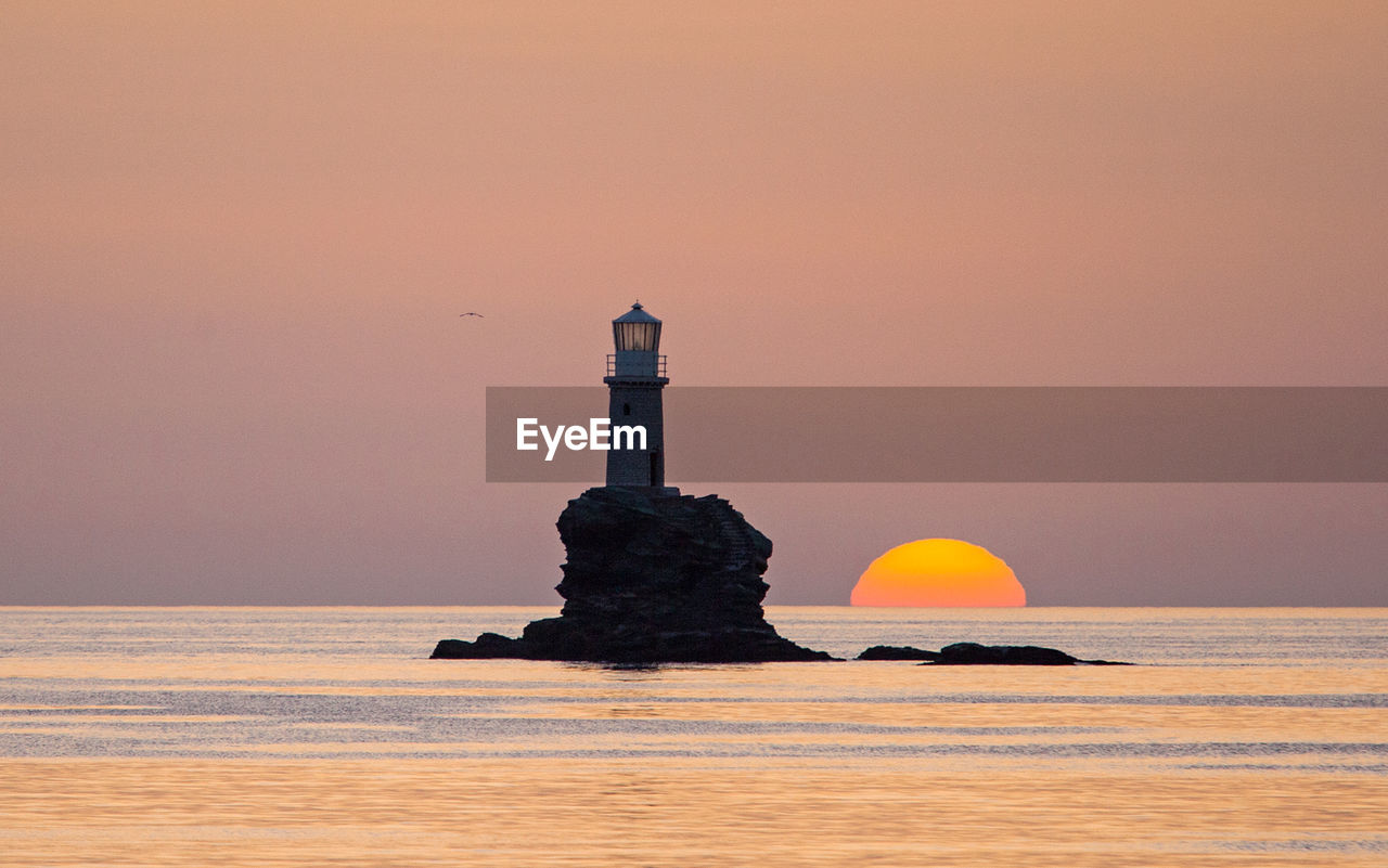 sunset, lighthouse, sea, tower, sky, water, ocean, horizon, nature, architecture, dawn, orange color, land, evening, guidance, no people, built structure, beauty in nature, beach, coast, scenics - nature, travel destinations, reflection, tranquility, travel, building, building exterior, outdoors, environment, security, landscape, silhouette, shore, protection, sand, sun, horizon over water, tranquil scene, copy space, seascape