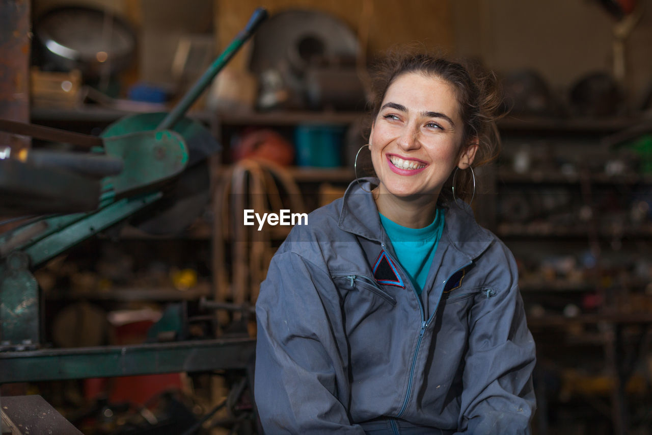 Smiling manual worker looking away while sitting in workshop