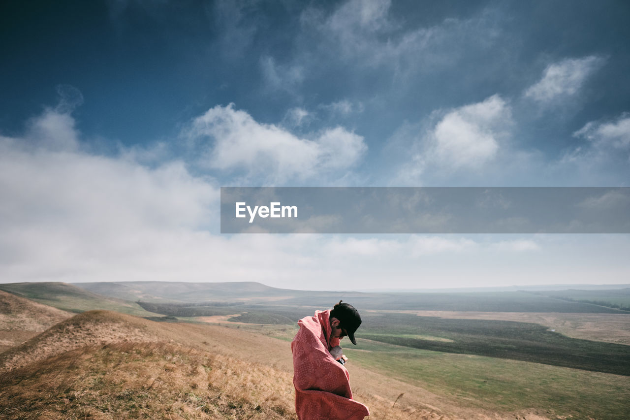 Side view of man standing on landscape against sky