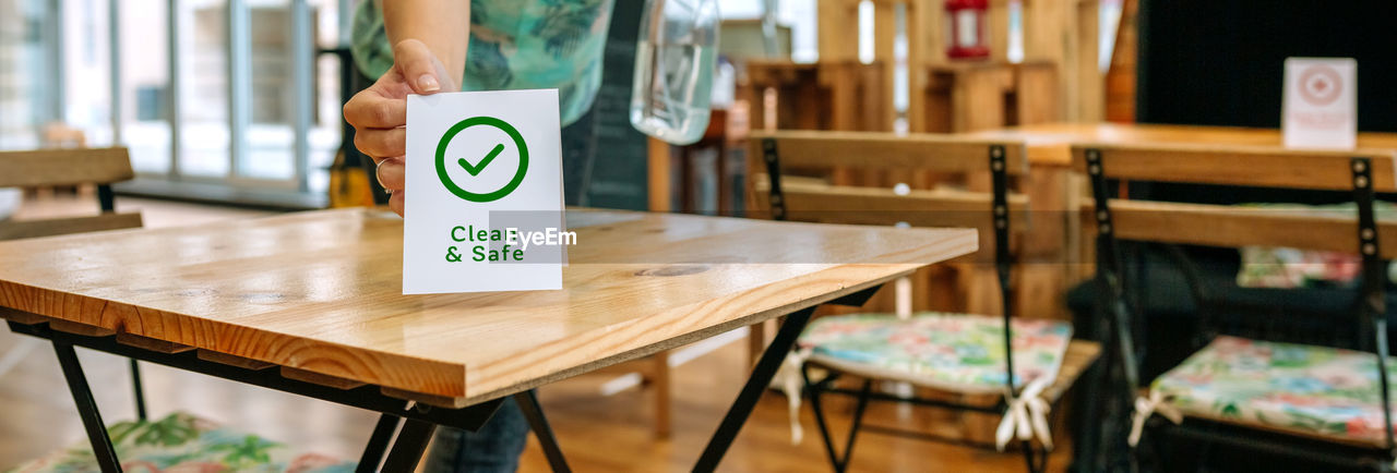 Unrecognizable waitress placing clean and safe sign on coffee shop table