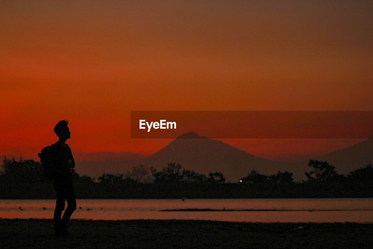 Silhouette man standing by sea against orange sky