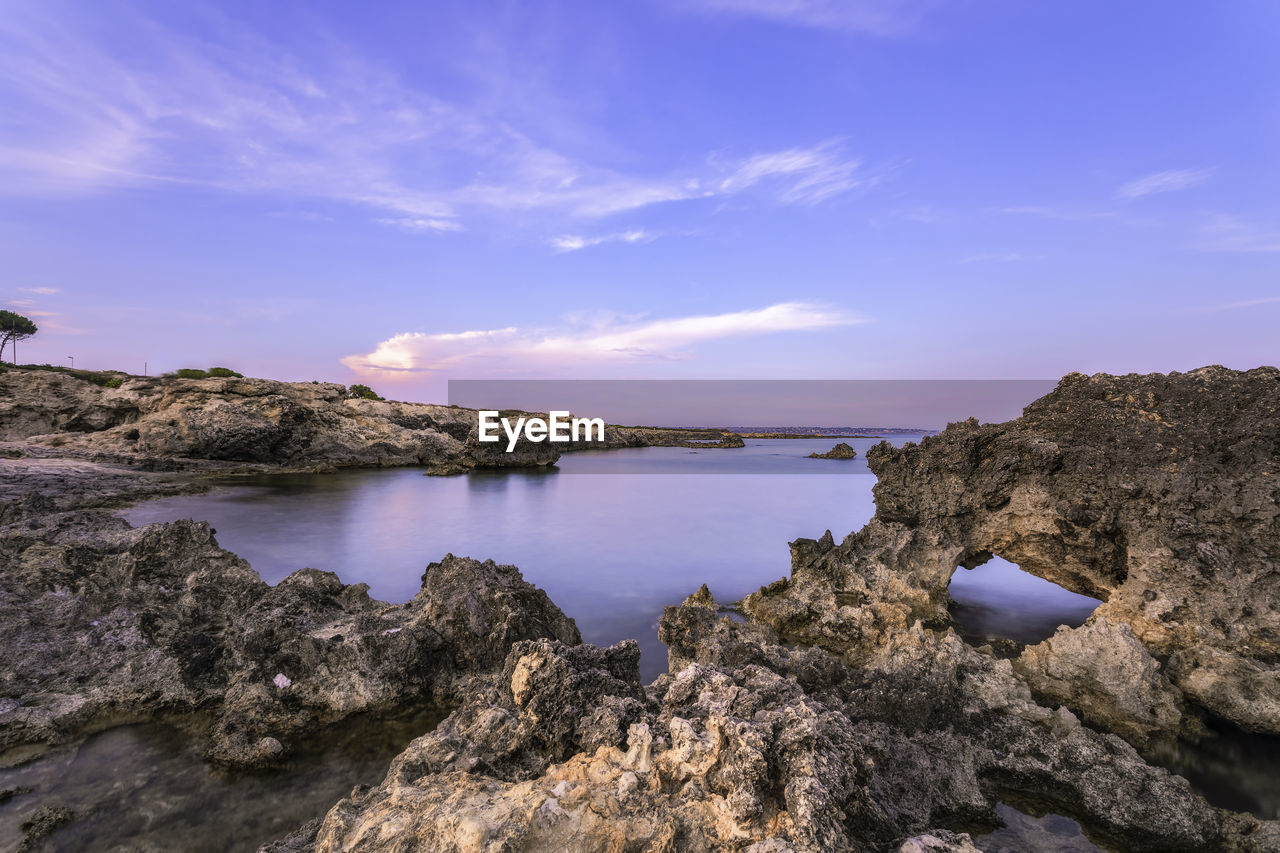 Rock formations by sea against sky during sunset