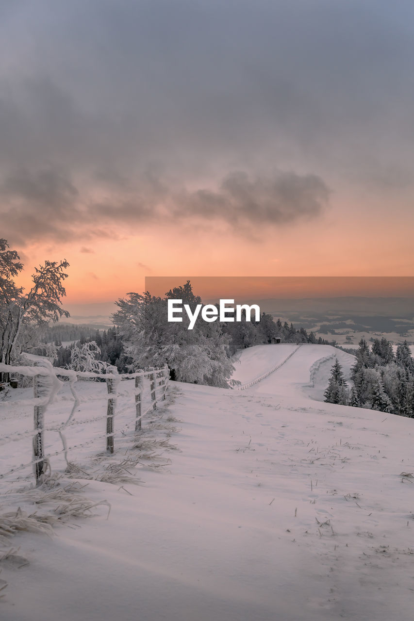 Snow covered field against sky during sunset