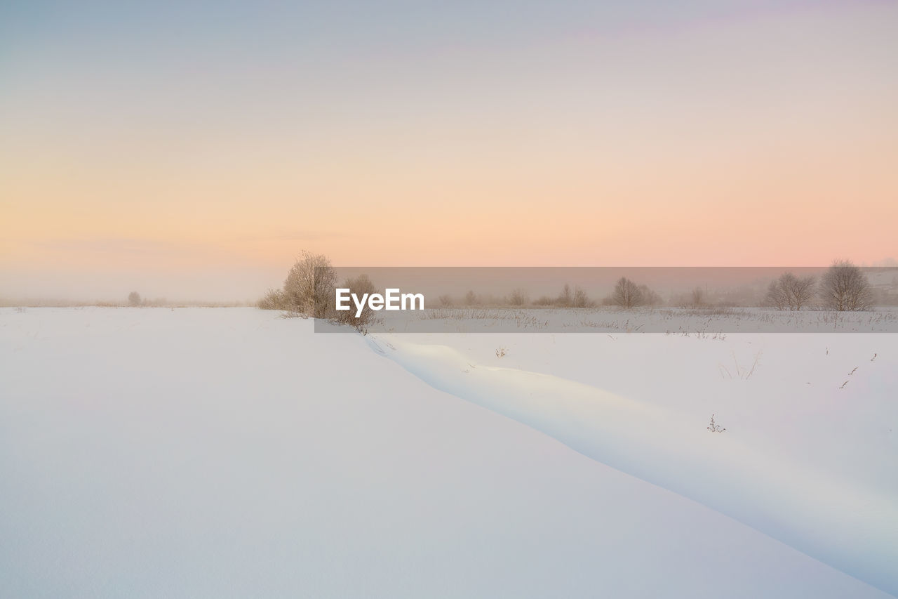 Scenic view of snow covered landscape against sky at sunset