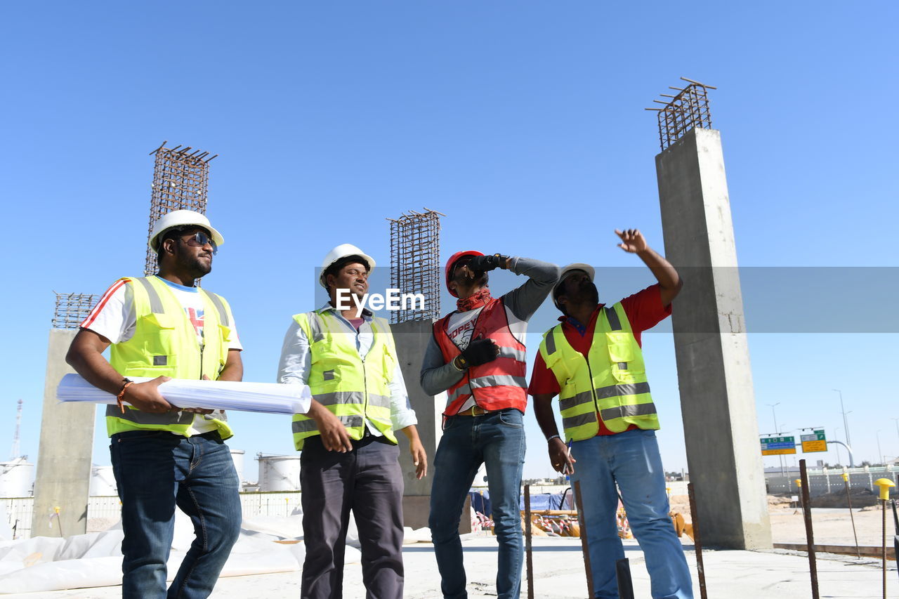 Low angle view of architects standing at construction site against clear blue sky