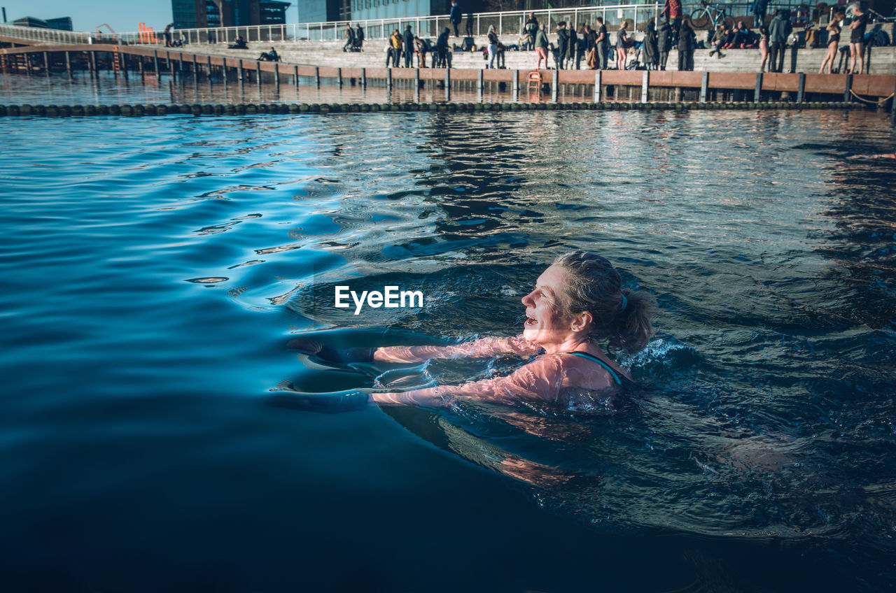 Mature woman swimming with sun shining in freezing water in denmark