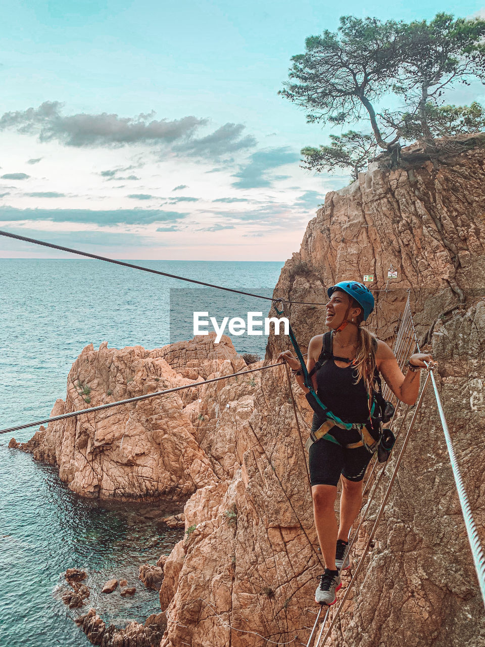 Smiling woman walking on rope bridge by sea against sky