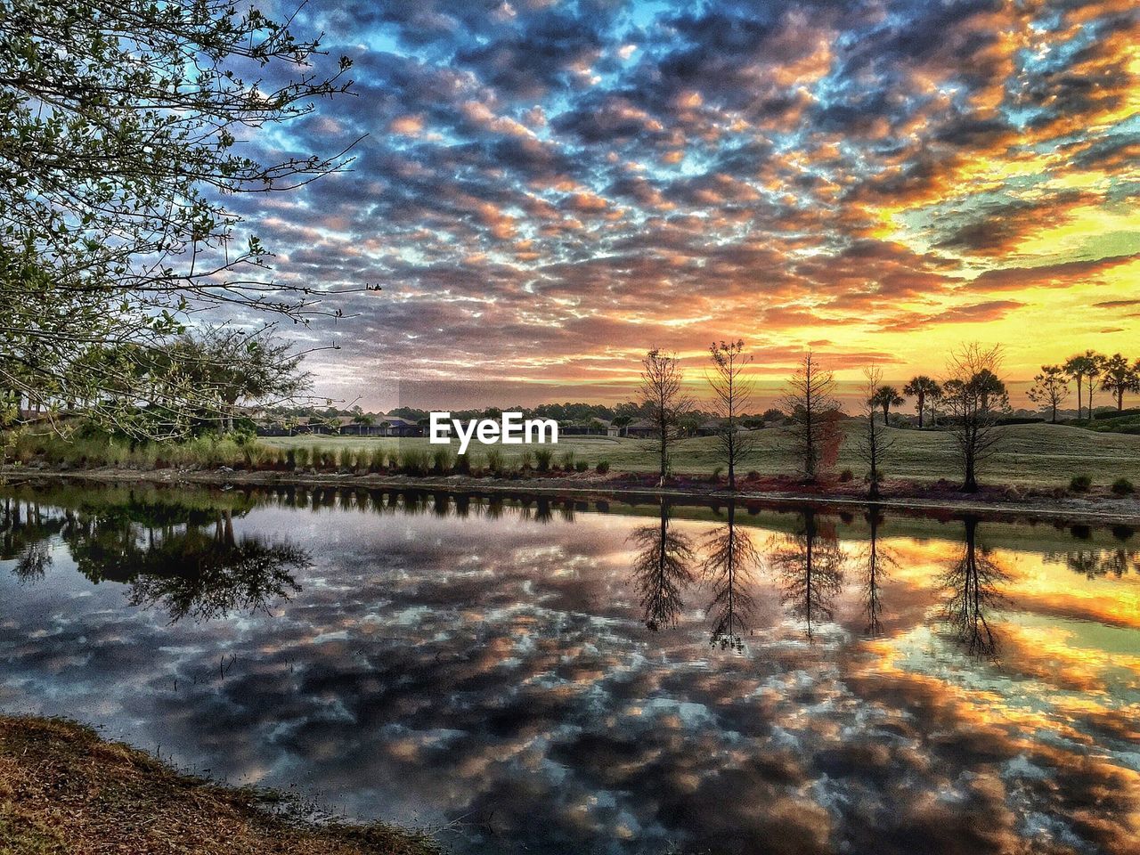 Scenic view of clouds reflecting in lake by field during sunset