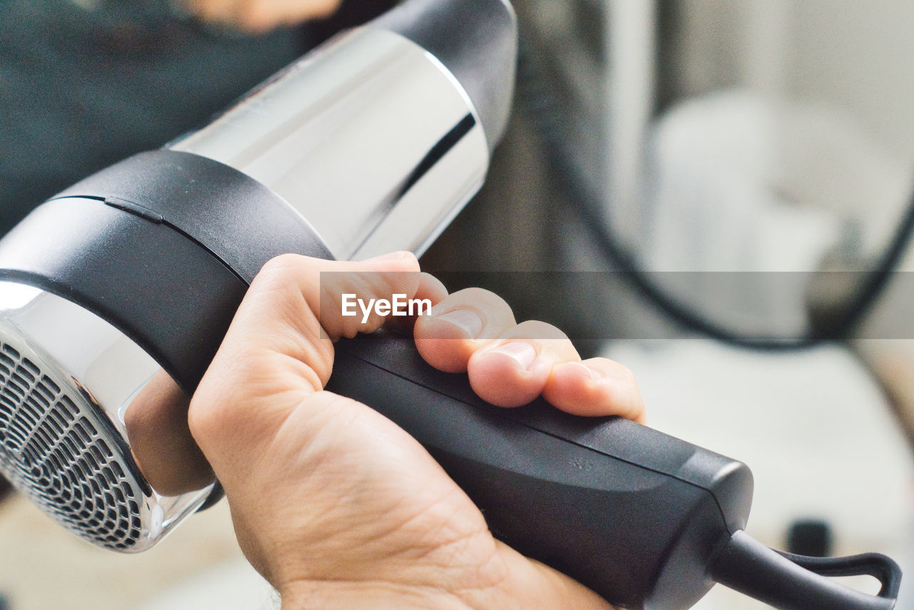 Cropped image of woman holding hair dryer indoors