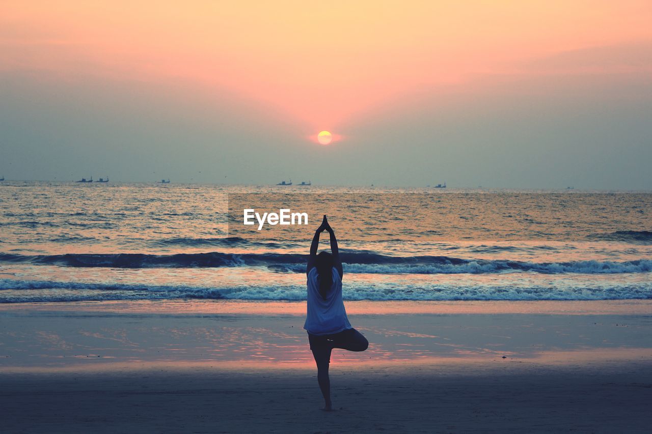 Rear view of woman doing yoga at beach during sunset