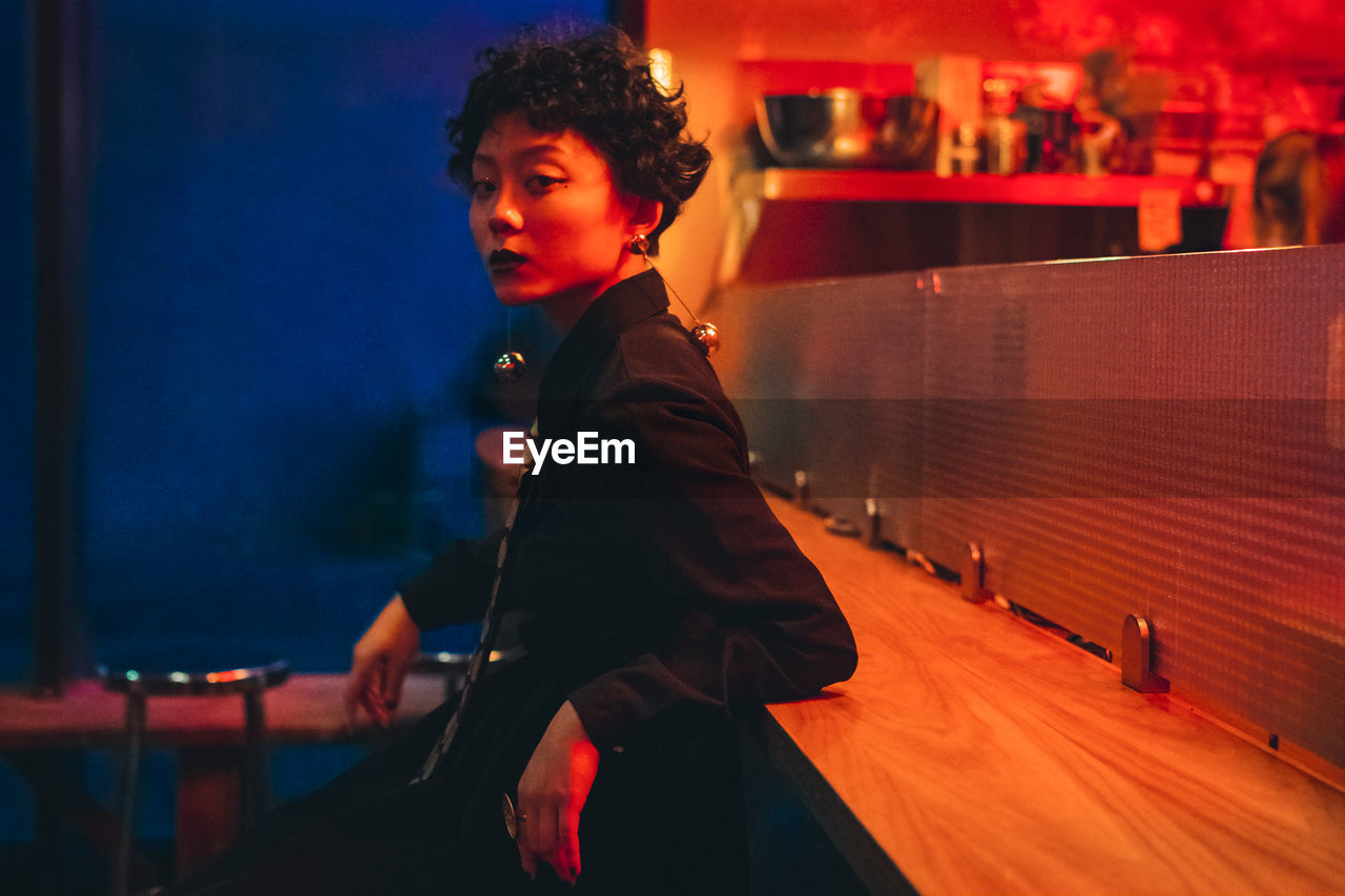 Portrait of woman looking away while sitting in illuminated nightclub