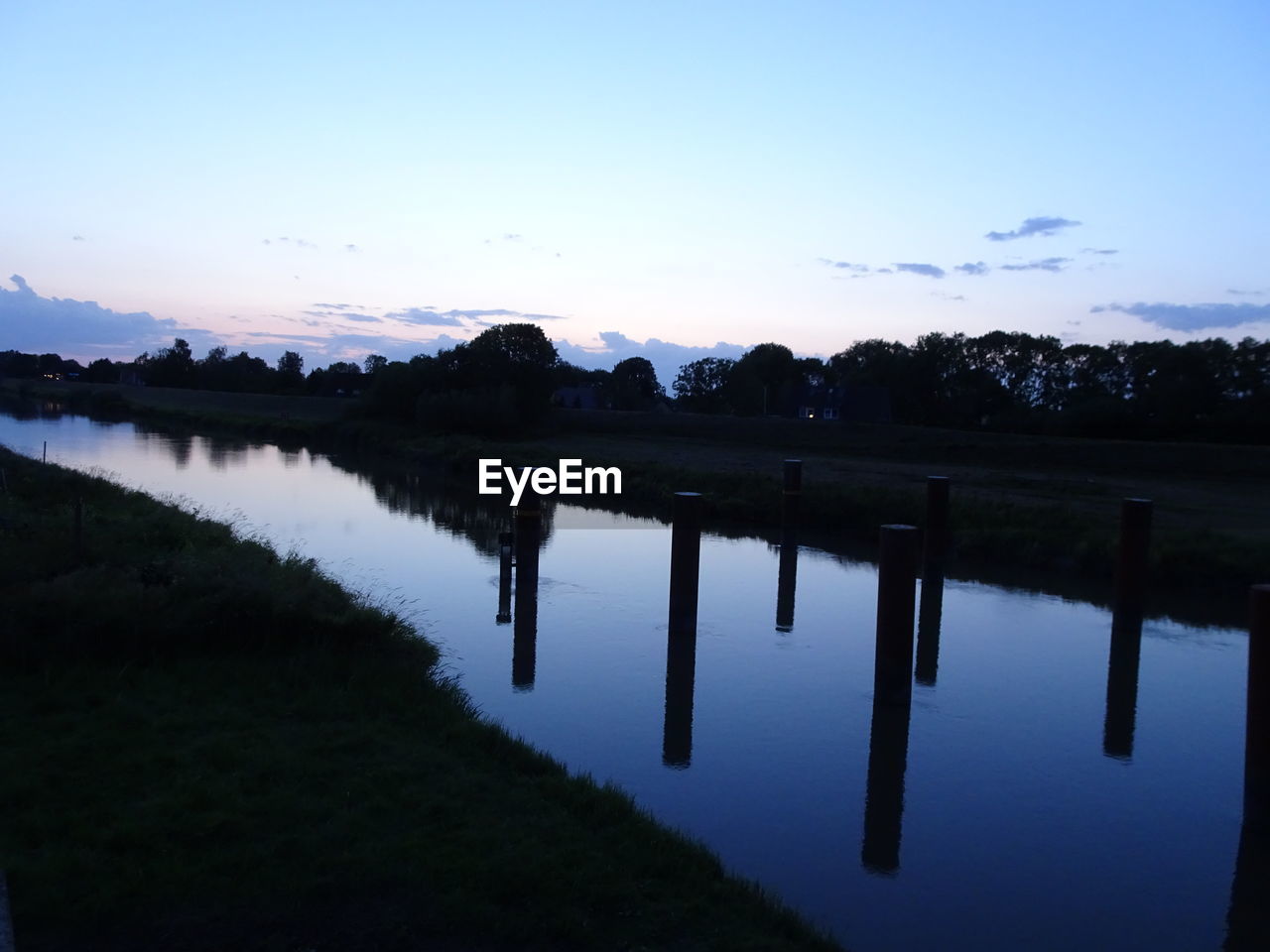 REFLECTION OF SILHOUETTE TREES IN LAKE AGAINST SKY AT SUNSET