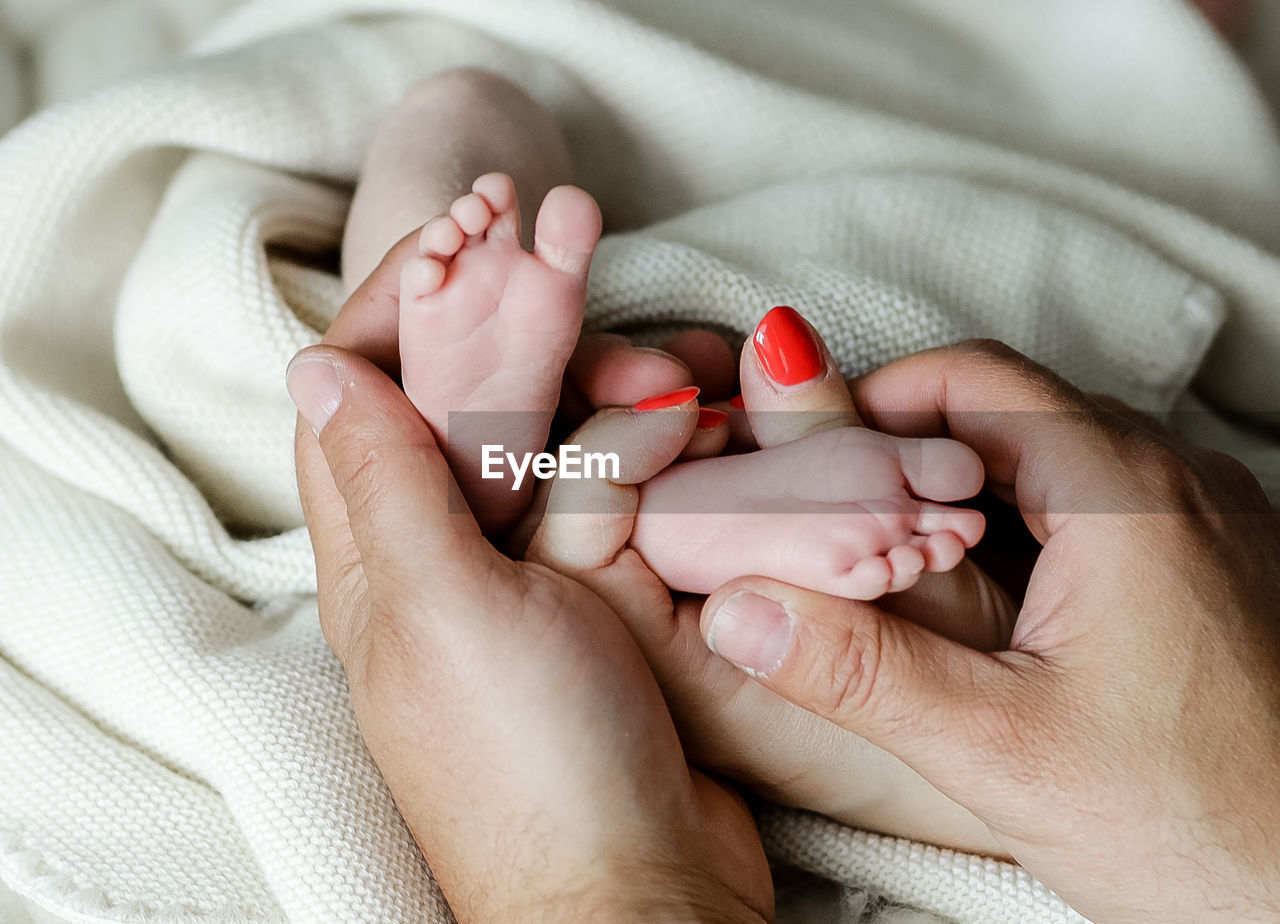 Cropped hands of people holding baby legs on bed