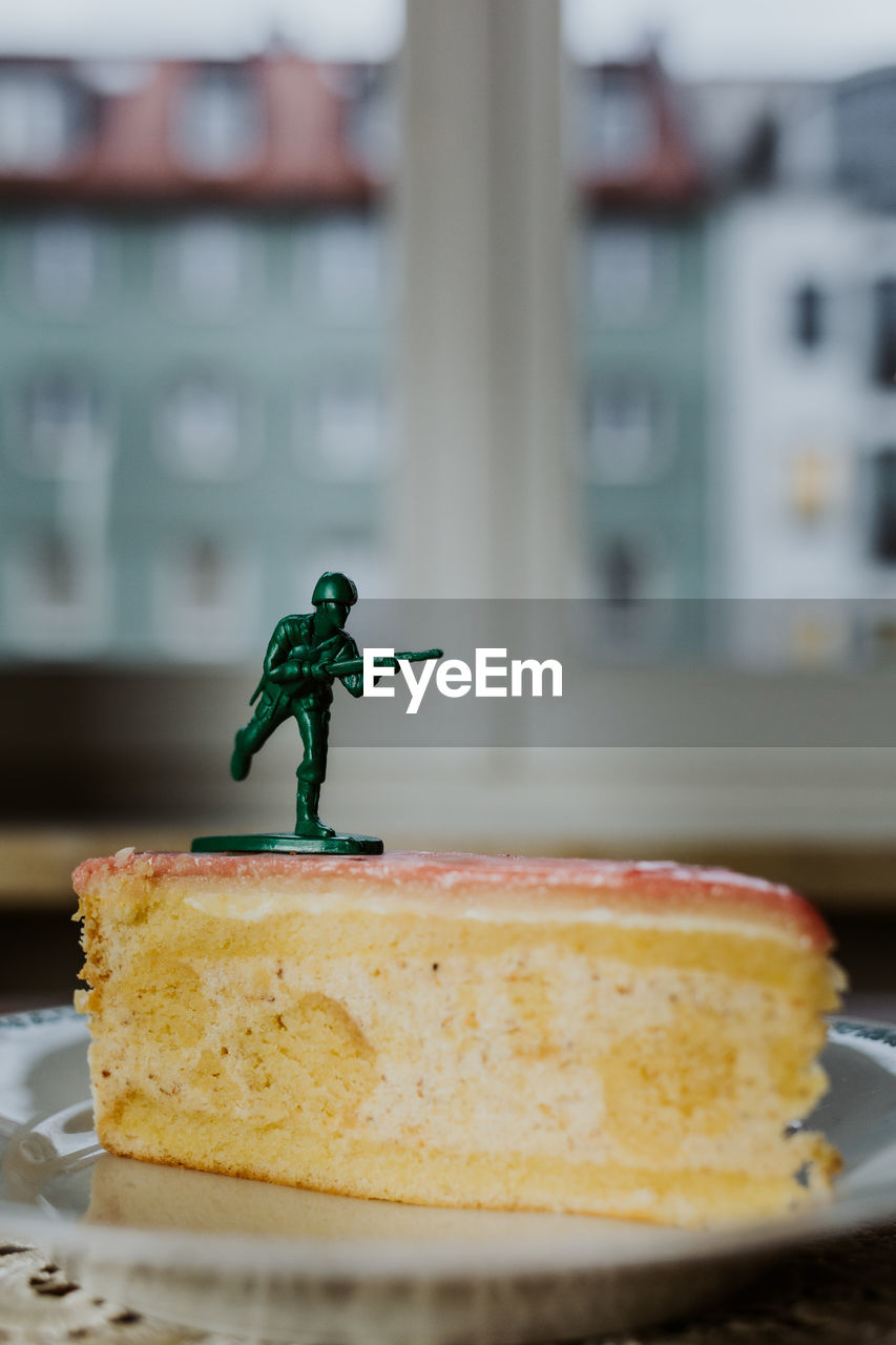 Toy soldier standing on the top of a piece of cake - close up of figurine aginst window background